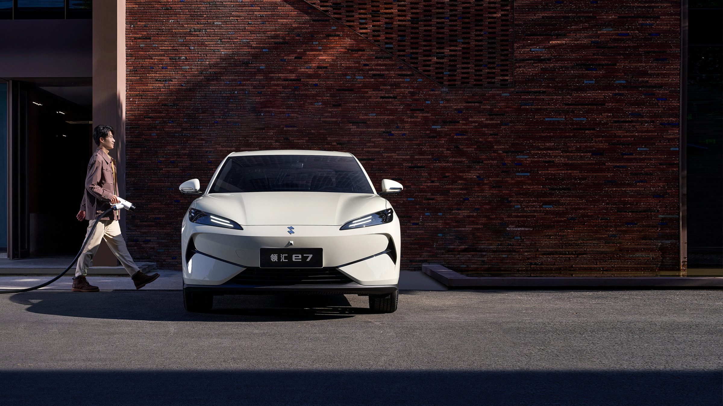 A driver walking past a Linghui e7 with a charging cable